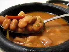 a spoon full of beans and carrots in a black bowl on a white table