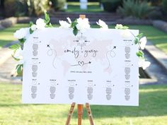 a wedding seating chart with white flowers and greenery around it on an easel