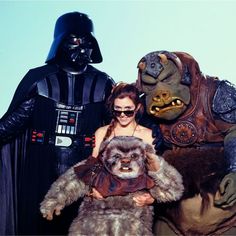 a woman standing next to two star wars characters and one is holding a stuffed animal