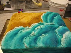 a cake with blue and yellow frosting sitting on top of a counter next to a cup