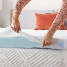 a woman is placing the mattress on top of the bed and pulling it out with her hands