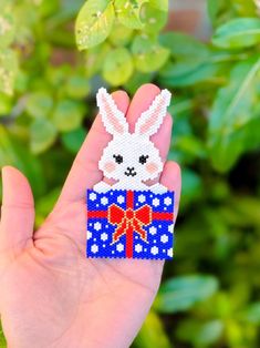 a hand holding a piece of bead art that looks like a bunny with a bow