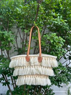 Discover the perfect blend of traditional craftsmanship and contemporary style with this stunning handmade Moroccan raffia bag. This beautiful piece features intricate woven patterns and eye-catching fringe detailing, showcasing the exceptional skill of Moroccan artisans. The bag is adorned with three tiers of elegant fringe, adding a playful yet sophisticated touch. Sturdy leather handles provide a comfortable carry, making it ideal for everyday use or special outings. Each bag is a unique creation, ensuring you have a one-of-a-kind accessory to complement any outfit. Features: *Artisan-crafted in Morocco *High-quality raffia material *Three tiers of fringe detailing *Durable leather handles *Unique, one-of-a-kind design Ideal For: *Beach trips *Shopping *Casual outings *Enhancing bohemia Bohemian Beige Beach Bag With Braided Handles, Tasseled Straw Shoulder Bag, Beach Shoulder Bag With Tassels, Rectangular Shape, Bohemian Bucket Bag With Tassels For Beach, Beige Tassel Beach Bag, Beige Tassel Bag For Beach, Bohemian Beige Woven Beach Bag, Beige Tassel Bag For The Beach, Summer Straw Shoulder Bag With Tassels