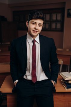 a young man in a suit and tie sitting at a desk with his hands on his hips