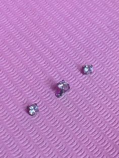 three diamond studs laying on top of a purple surface with white dots in the middle