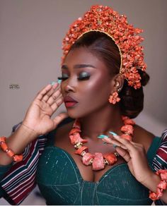 an african woman in a green dress with orange flowers on her head and hands near her face