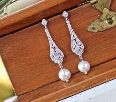 two pairs of pearl and diamond earrings sitting on top of a wooden box next to a key