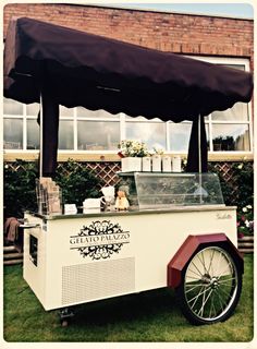 an ice cream cart sitting on top of a lush green field next to a tall brick building