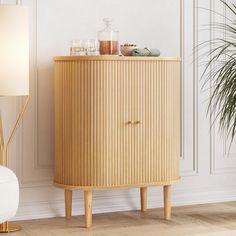 a wooden cabinet sitting next to a white chair in a room with a lamp on the floor