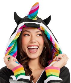 a woman wearing a rainbow unicorn hat and holding her hands up to her ears while smiling at the camera