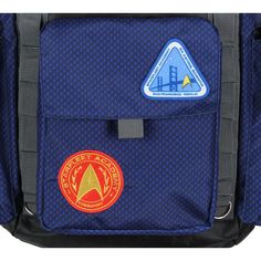 This Star Trek backpack is for all your space travels! It features an embroidered Starfleet Academy insignia. The backpack features several patches with the same Starfleet Academy logo as pictured throughout the years on the show. On one of the sides, it features "Est. 2161." The backpack features many cargo-style pockets, including dual side pockets and a smaller one on the front for fitting all your Star Trek merchandise! It also features an inner laptop sleeve in the main backpack and a roll- Blue Travel Bag With Logo Patch, Starfleet Academy, Star Trek Merchandise, Academy Logo, Cargo Style, Roll Top, Blue Backpack, Travel School, Space Travel