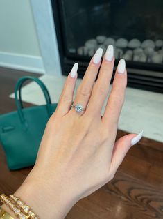 a woman's hand with white nail polish holding a diamond ring in front of a fireplace