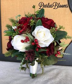 a bridal bouquet with red and white flowers, greenery and berries is displayed in front of a wall