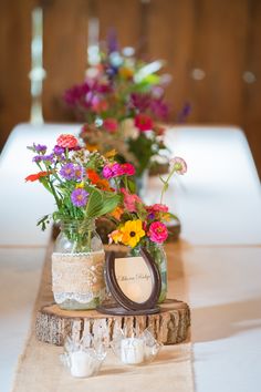 colorful flowers in vases sitting on top of a wooden log at a wedding reception