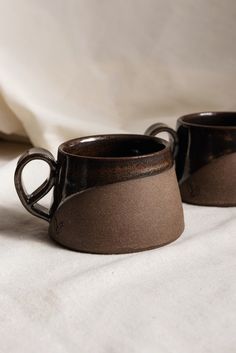 two brown cups sitting on top of a white bed sheet next to eachother