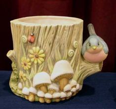 a ceramic bird sitting on top of a tree stump next to mushrooms and daisies