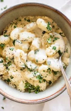 a bowl filled with macaroni and cheese covered in herbs next to a spoon