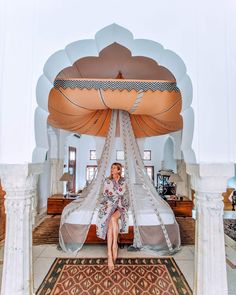 a woman sitting on top of a bed in a room with white walls and columns