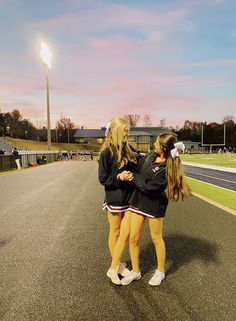 two young women standing on the side of a road next to each other with their arms around each other