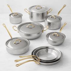 an assortment of pots and pans with gold handles on a white countertop top