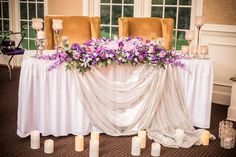 a table with candles and flowers on it in front of two chairs at the end