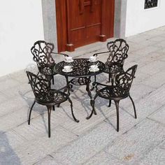 an outdoor table and four chairs on the sidewalk with a door in the back ground