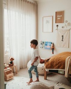 a young boy standing in his bedroom looking out the window