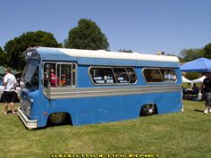 an old blue bus is parked in the grass with people standing around and looking at it