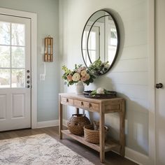 a wooden table with flowers and baskets on it in front of a white door that has a round mirror above it