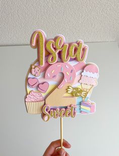 a hand holding up a pink and gold cake topper that says 1 year sweet