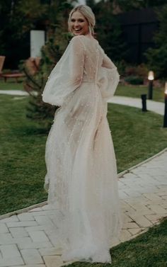 a woman in a white dress standing on a brick walkway with her arms behind her back