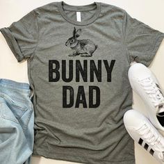 Bunny Dad short-sleeve crewneck t-shirt. Unisex Fit. Printed with eco-friendly water-based inks. Please refer to the size chart in the last image of the listing (laying flat measurements in inches). Due to the calibration differences between computer monitors, phone screens and tablets, the actual product color may vary slightly from what you are viewing.SHIRT FEATURES:- 4.2 oz., Solid color tees (red, white, blue, green) are 100% combed and ringspun cotton, 30 singles- Athletic Heather Shirt (l Dad Shorts, Funny Easter, Easter T Shirts, Funny Gifts For Dad, Funny Dad Shirts, Easter Humor, Phone Screens, Yoga Tops, Charcoal Color