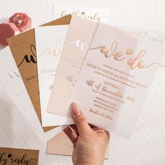 a person holding up some paper with gold foil on it and pink flowers in the background