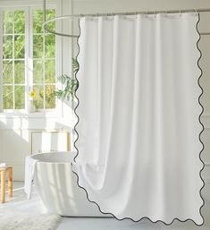 a white shower curtain with scalloped edges in front of a bathtub and window