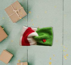 a green and white knitted hat with a red heart on it next to presents