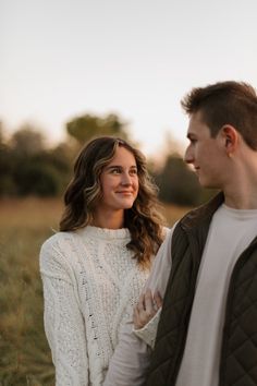 a young man and woman are standing together in the grass looking into each other's eyes