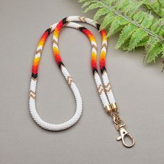 a white and orange leash with gold hardware on a gray surface next to a fern