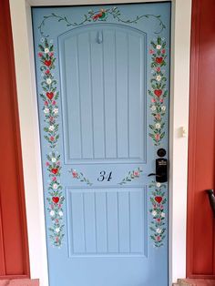 a blue front door decorated with flowers and numbers on the side wall is painted red