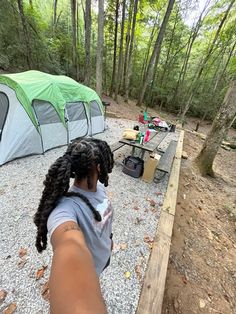 a woman standing next to a tent in the woods