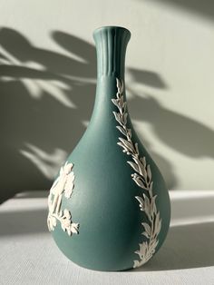 a green vase sitting on top of a table next to a shadow cast by the wall