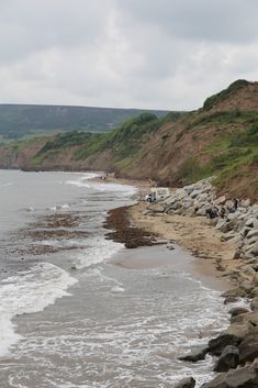 people are standing on the edge of a cliff overlooking the ocean and rocky shore line