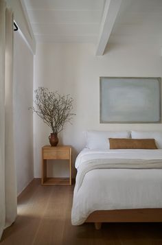 a white bed sitting in a bedroom next to a wooden table with a potted plant on it