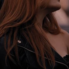 a woman with red hair is looking off into the distance while wearing a leather jacket