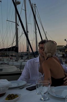 a man and woman sitting at a table in front of sailboats