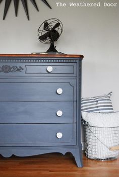 a blue dresser sitting on top of a hard wood floor next to a wall clock