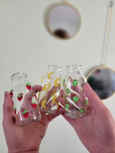 two hands holding three small glass vases with designs on the bottom and one is filled with liquid