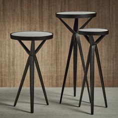 two black tables sitting next to each other on top of a cement floor in front of a wooden wall