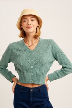 a woman in a green sweater and hat poses for the camera with her hands on her hips