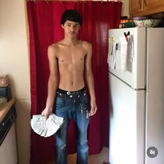 a shirtless young man standing in front of a refrigerator holding money and looking at the camera