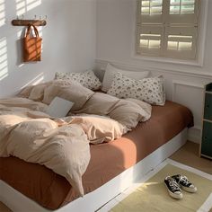 an unmade bed in a bedroom next to a window with shutters and shoes on the floor